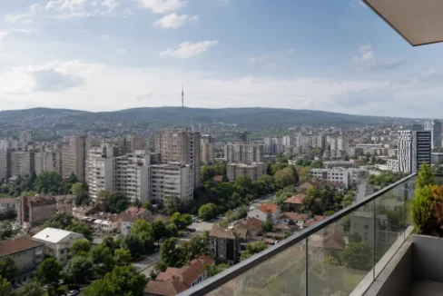 Pogled na Voždovac u Beogradu sa stambenim zgradama, zelenilom i Avalom u daljini, kao ilustracija teksta o cenama stanova na Voždovcu u 2026. godini.